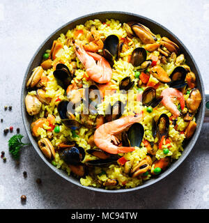 Traditionelle spanische Paella in der Pfanne Reis, Erbsen, Krabben, Muscheln, Tintenfisch auf Hellgrau konkreten Hintergrund. Ansicht von oben, Copyspace. Stockfoto