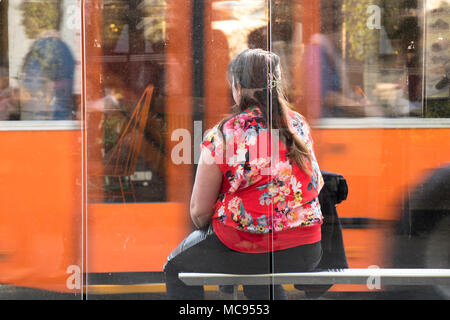 Belgrad, Serbien - 11. April 2018: Eine Frau an der Bushaltestelle sitzen warten und eine orange Verkehr hinter Ihr Umzug Stockfoto