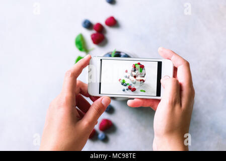 Mädchen ist Fotos von Frühstück, Chia Milchreis mit Beeren zu Mobiltelefon. Social Media, Instagram Konzept. Kopieren Sie Raum, Ansicht von oben Stockfoto