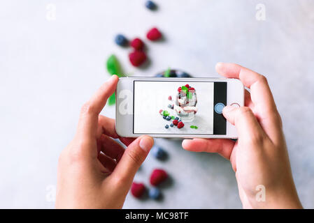Mädchen ist Fotos von Frühstück, Chia Milchreis mit Beeren zu Mobiltelefon. Social Media, Instagram Konzept. Kopieren Sie Raum, Ansicht von oben Stockfoto