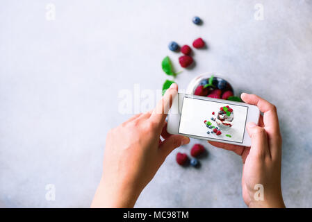 Mädchen ist Fotos von Frühstück, Chia Milchreis mit Beeren zu Mobiltelefon. Social media Konzept. Kopieren Sie Raum, Ansicht von oben Stockfoto