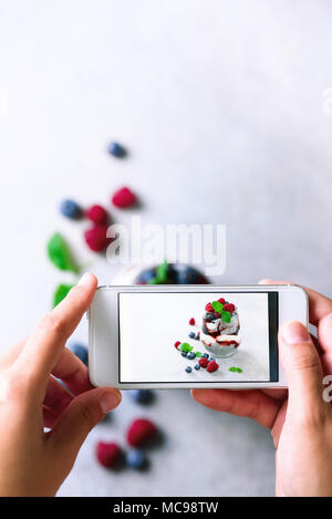 Mädchen ist Fotos von Frühstück, Chia Milchreis mit Beeren zu Mobiltelefon. Social media Konzept. Kopieren Sie Raum, Ansicht von oben Stockfoto