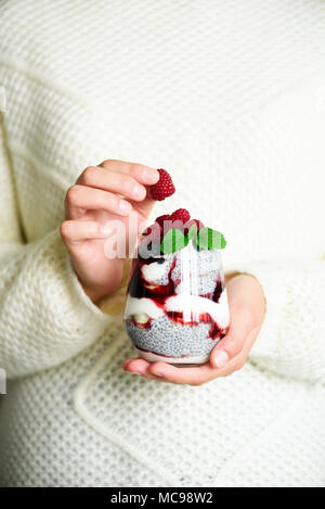 Mädchen in weißen Pullover hält Glas mit Chia Milch Nachtisch, Himbeeren, Heidelbeeren, Minze. Gesundes Frühstück Konzept. Platz kopieren, Nahaufnahme Stockfoto