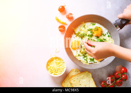 Sonnigen morgen. Frühstück mit Spiegelei in der Pfanne, Kräuter, Gewürze, Tomaten, Käse, Toast, Basilikum auf grauem Beton Stein Hintergrund. Platz kopieren, t Stockfoto