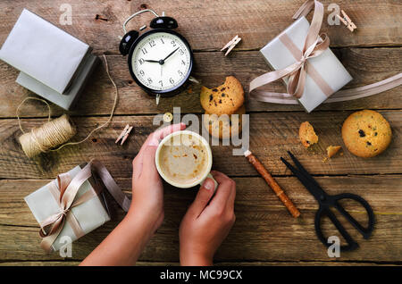 Schöne Frau Hände halten Geschenkbox auf Holz- Hintergrund. Schwarz Wecker, Stift, Schere. Vorbereitung für Geburtstag, Weihnachten, neues Jahr. Lebensstil Stockfoto