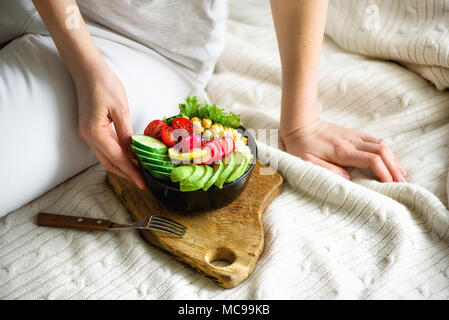 Mädchen in den Händen hält, vegan, Detox raw Buddha Schüssel mit Avocado, Quinoa, Gurken, Radieschen, Salat, Zitrone, Cherry Tomaten, Kichererbse, Chia Samen auf Textilien Stockfoto