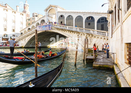 Venedig, Italien - Juni, 21, 2013: Blick auf die Gondeln mit Passenges und Ponte di Rialto, viele Touristen auf einer Brücke,, Openair Restaurant mit Sonnenschirmen auf Stockfoto