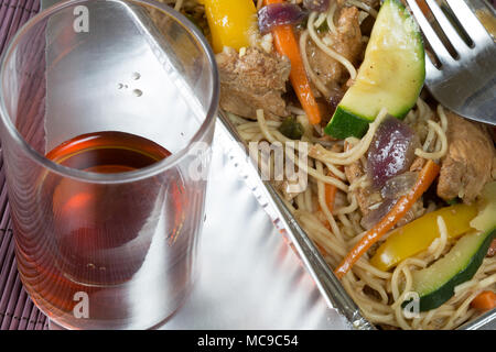 Chinesisch Takeaway der Chicken Nudel Rühren braten in einer Folie Lieferung Gericht mit einem Glas von Saki Stockfoto