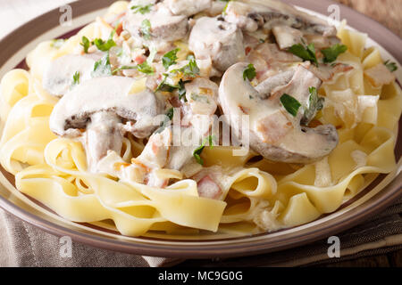 Italienische Pasta Fettuccine mit cremiger Sauce, Champignons, Speck und Zwiebeln closeup auf einem Teller auf dem Tisch. Horizontale Stockfoto