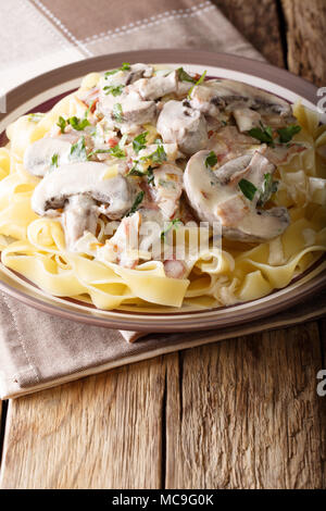 Pasta Fettuccine mit Sahne, Champignons, Speck und Zwiebeln close-up auf einem Teller auf dem Tisch. Vertikale Stockfoto