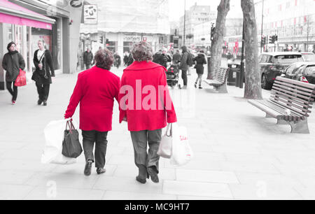 Zwei unkenntlich alte Damen Frauen tragen ein helles Rot winter Jacke zu Fuß auf einer belebten Hauptstraße mit Einkaufstaschen Stockfoto