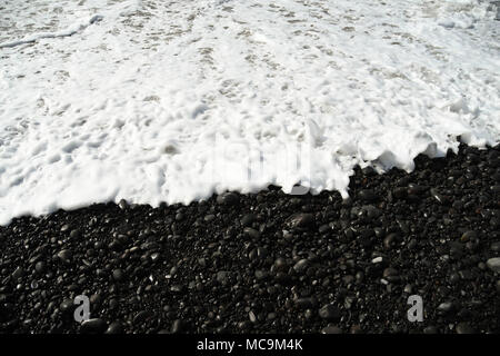 Weißer Schaum aus der Flut auf der schwarzen vulkanischen Strand Stockfoto