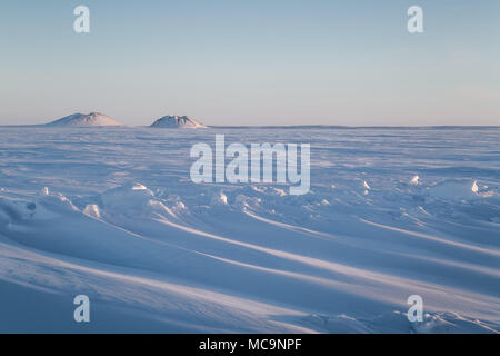 Schneeverwehungen mit Pingos (Intra-Permafrost-eisbewachsenen Hügeln) in der Ferne, in der Nähe des arktischen Weilers Tuktoyaktuk, Northwest Territories, Kanada. Stockfoto