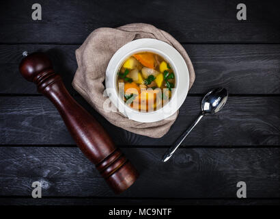 Shurpa mit Lamm und Gemüse, in weiße Schüssel mit dem Löffel, Serviette und Pepper Grinder auf der hölzernen Hintergrund serviert. Ansicht von oben. Stockfoto