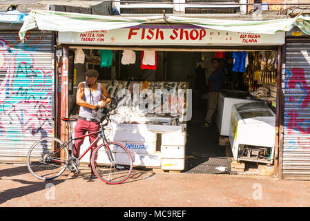 Kleine lokale unabhängige Fish shop Fischhändler in Ridley Road Market mit Kunden auf dem Fahrrad anhalten im Herzen von Dalston, East London, Stockfoto