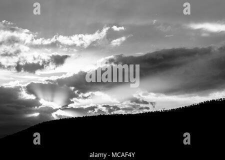 Sonnenuntergang über einem Bäume Linie auf einem Hügel, mit Sonnenstrahlen, die sich durch einige Wolken Stockfoto