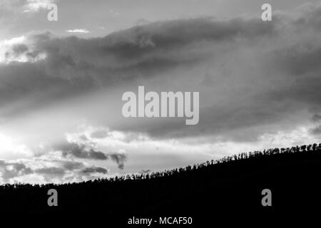 Sonnenuntergang über einem Bäume Linie auf einem Hügel, mit Sonnenstrahlen, die sich durch einige Wolken Stockfoto