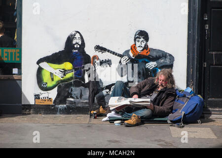 Ein Mann entspannt auf dem Bürgersteig in Soho, vor einem Bild von John Lennon und Paul McCartney Stockfoto