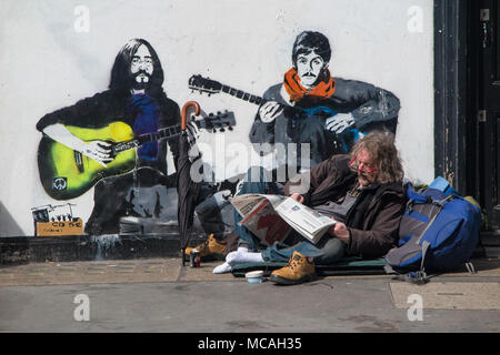 Ein Mann entspannt auf dem Bürgersteig in Soho, vor einem Bild von John Lennon und Paul McCartney Stockfoto