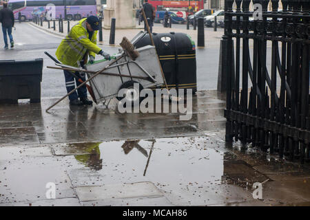 Eine Straßenkehrmaschine Entleerung ein bin ist in eine Pfütze auf einem regnerischen London Street wider Stockfoto