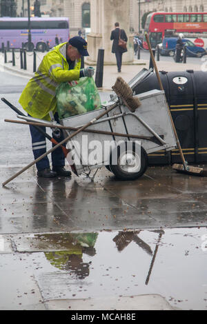 Eine Straßenkehrmaschine Entleerung ein bin ist in eine Pfütze auf einem regnerischen London Street wider Stockfoto