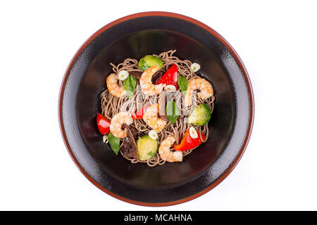 Buchweizen Nudeln mit Garnelen und Teriyaki Sauce, auf weißem Hintergrund. Buchweizen Nudeln in eine schwarze Platte. Platte der ungewöhnliche Form. Stockfoto