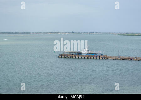 Blaue und weiße Boot Transportieren von Personen nicht mehr in den alten Hafen, Hintergrund mit tropischen Insel und grau blauer Himmel Stockfoto