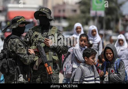 Gaza, Palästina. 15 Apr, 2018. Palästinensische Schulkinder vorbei eine militante Wache in der Straße bei der Beerdigung des Islamischen Djihad Militanten, welche bei einer Explosion getötet wurden, in Rafah im südlichen Gazastreifen, 15. April 2018. Al-Quds-Brigaden, der bewaffnete Arm der Palästinensischen Islamischen Dschihad Organisation, sagte, dass vier seiner Kämpfer während einer Mission der militärischen Einrichtung, Zubereitungen und Verarbeitung getötet wurden. Foto: Wissam Nassar/dpa Quelle: dpa Picture alliance/Alamy leben Nachrichten Stockfoto