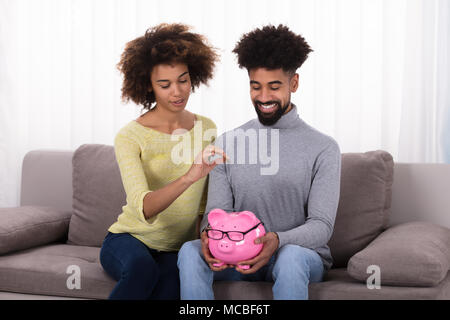 Glückliches Paar sitzt auf einem Sofa einfügen Münze in Sparschwein Stockfoto