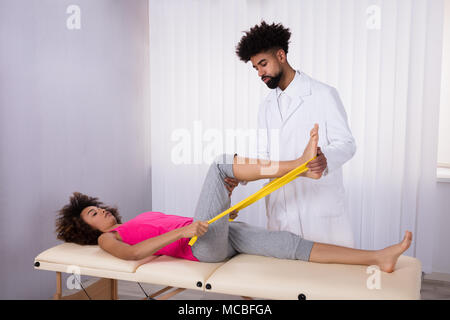 Junge männliche Physiotherapeuten helfen weiblichen Patienten, während Ihr Bein Dehnen in Klinik Stockfoto
