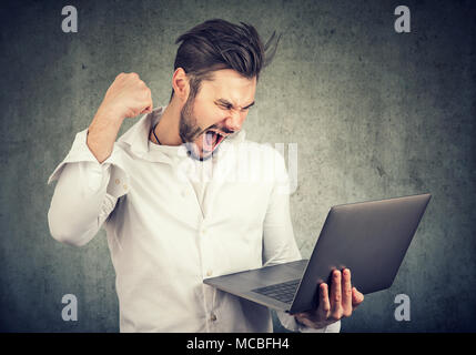 Neugierige junge Mann mit Laptop und suchen gerne gewinnen mit höchster Leistung. Stockfoto