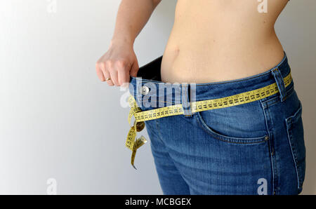 Gewicht-verlust-Konzept. Frau zeigt Ihr Gewicht Verlust durch das Tragen einer alten Jeans. Gesunder Lebensstil, Diät Konzept mit übergroßen Jeans. Stockfoto