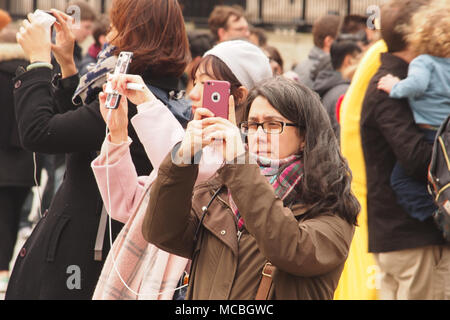 Drei junge Frauen, die selfies auf ihren Smartphones in einer Menschenmenge auf dem Trafalgar Square, London Stockfoto