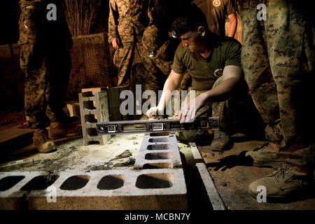 Lance Cpl. Joseph Dickens, eine Bekämpfung der Ingenieur mit 1 Platoon, Co.9. Unterstützung der Techniker Bataillon, 3. Marine Logistik Gruppe, legt Steine in den späten Abend März 26, 2018, Camp Hansen, Okinawa, Japan. Die Marines waren auf dem Feld bis zum Bau eines Munition Lagerung Punkt abgeschlossen wurde, können Sie über Ihre Sicherheit Fahrzeug und Scheinwerfer bis spät in die Nacht zu sehen. Vertikalen Aufbau Schulung bereitet Marines für ähnliche Projekte, die Sie mit während der humanitären Hilfsmaßnahmen übertragen werden. Dickens ist ein Eingeborener von Beckley, West Virginia. Stockfoto