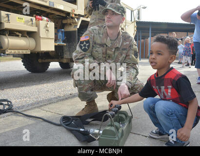 Jayquan Roberts, ein pre-kindergarten Student an der Walton Elementare, drückt Hebel ein Kran auf eine Armee schwere Erweiterte Mobilität Tactical Truck mit Staff Sgt. Kyle McGovern, ein radfahrzeug Mechaniker, 111 Quartermaster Unternehmen, während der Schule Wissenschaft, Technologie, Ingenieurwesen, Kunst und Mathe tag März 29. Soldaten aus Charlie Company, 16 Ordnance Battalion - Staff Sgt. Yolanda Walker, platoon Sergeant, und 1 Sgt. Mindy Shearin, Firma first Sergeant - Die statische Darstellung von der 111 QM-Co für ihre Adopt-a-School DAMPF Programm an die Schüler, wie die HEMTT ist in Show Stockfoto