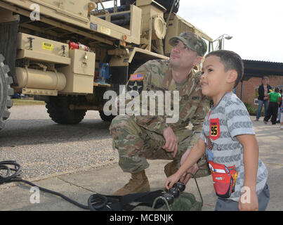 Ismael Ortiz, eine Pre-kindergarten Student an der Walton Elementare, drückt Hebel ein Kran auf eine Armee schwere Erweiterte Mobilität Tactical Truck mit Staff Sgt. Kyle McGovern, ein radfahrzeug Mechaniker, 111 Quartermaster Unternehmen, während der Schule Wissenschaft, Technologie, Ingenieurwesen, Kunst und Mathe tag März 29. Soldaten aus Charlie Company, 16 Ordnance Battalion - Staff Sgt. Yolanda Walker, platoon Sergeant, und 1 Sgt. Mindy Shearin, Firma first Sergeant - Die statische Darstellung von der 111 QM-Co für ihre Adopt-a-School Dampf die Schüler wie die HEMTT ist invol zu zeigen Stockfoto