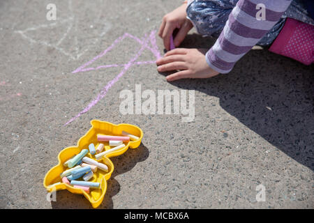 Das Kind Zeichnen einer Kreide auf Asphalt. Kasten mit farbigen Kreiden Stockfoto