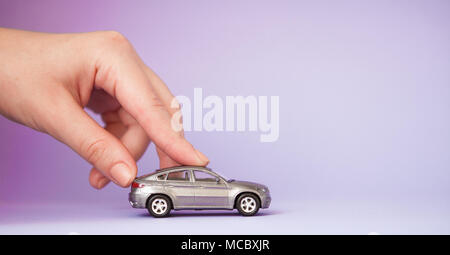 Spielzeug kind Auto in der Hand der Frau. Kauf Versicherungen Bank Kredit reisen wo Reise Reise Konzept zu gehen. Auf violett isoliert. Stockfoto