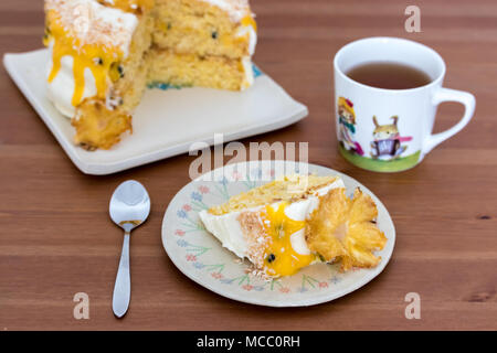 Eine Scheibe Ananas und Kokos Kuchen mit Passionsfrucht Quark, auf handgefertigten Teller serviert mit schwarzem Tee. Stockfoto