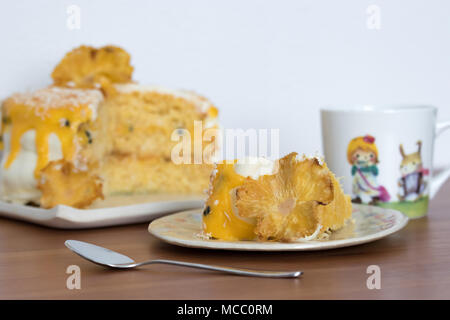 Tee am Nachmittag. Eine Scheibe Ananas und Kokosnuss Layer Cake mit Passionsfrucht Quark. Auf handgefertigten Teller serviert. Stockfoto