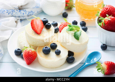 Mini Käsekuchen mit frischen Erdbeeren und Heidelbeeren auf blauen Platte, Detailansicht. Syrniki, Quark Pfannkuchen Stockfoto
