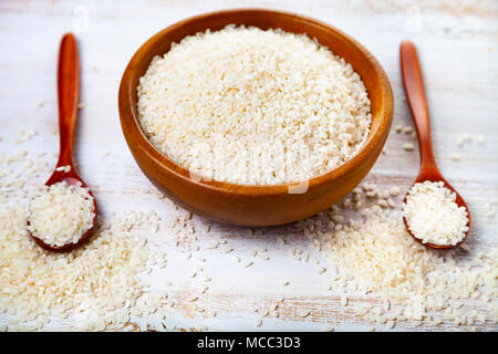 Raw gedämpftem Reis in eine Schüssel geben und zwei Löffel auf einer hölzernen Hintergrund. Zutaten für eine gesunde Ernährung. Stockfoto