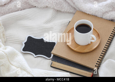 Tasse Kaffee auf das alte Buch und leere Schiefertafel über gemütliche und weiße Decke. Ansicht von oben Stockfoto