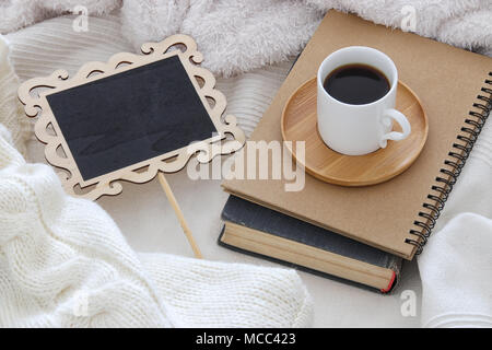 Tasse Kaffee auf das alte Buch und leere Schiefertafel über gemütliche und weiße Decke. Ansicht von oben Stockfoto