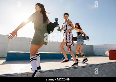 Drei weibliche Freunde laufen und springen über Skate park Rampe. Frauen Skater genießen Skate Park. Stockfoto