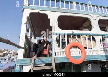 Frau in einem langen schwarzen Kleid sitzt auf dem Deck eines alten Holzboot. Stockfoto