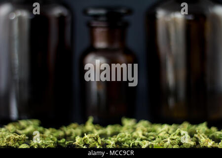 Cannabisknospen und Blumen mit alten Apothekenflaschen auf schwarzem Hintergrund. Stockfoto