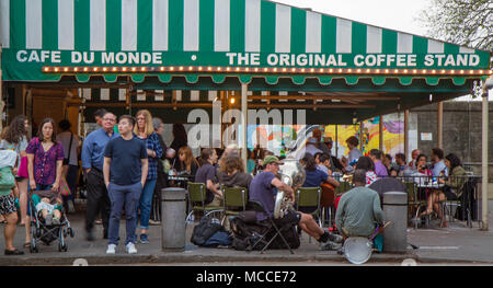 Café Du Monde, New Orleans, Louisiana, USA. Eine Menschenmenge vor dem berühmten Café neben einer Brass Band, goldenes Licht auf Markise. Stockfoto