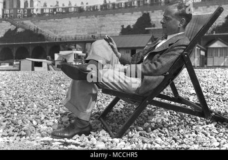 Ende der 1940er-Jahre, historische, einem gut gekleideten Gentleman genießt eine Zigarette und ein Nickerchen - ein wenig geschlossen - Auge - beim Entspannen auf seinem eigenen in einem Liegestuhl sitzen auf einem Kieselstrand, England, UK. Stockfoto