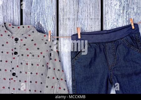 Jungen Kleidung trocknen auf Seil. Little boy Jeans und T-Shirt hängen auf wäscheleine auf alten Holz- Hintergrund. Kinder Kleid in Wäsche. Stockfoto